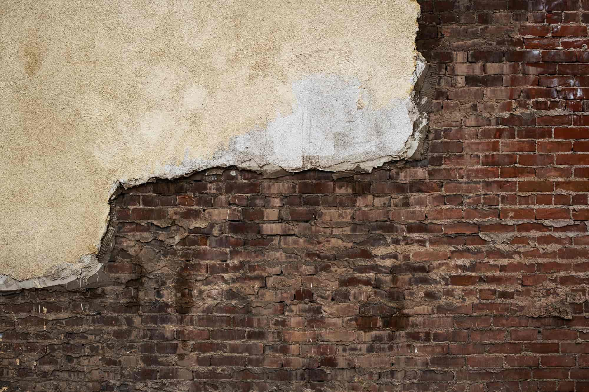 Broken exterior render exposing red brick underneath