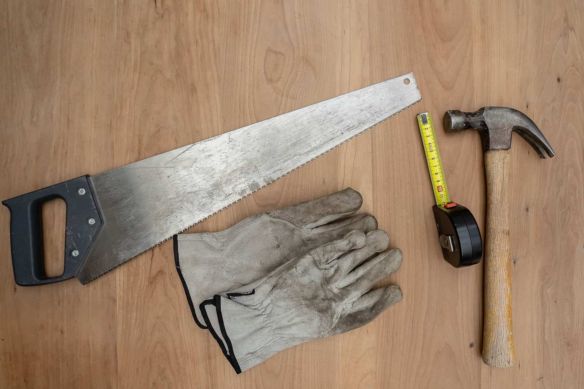 Hand saw, work gloves and a hammer on a wooden surface