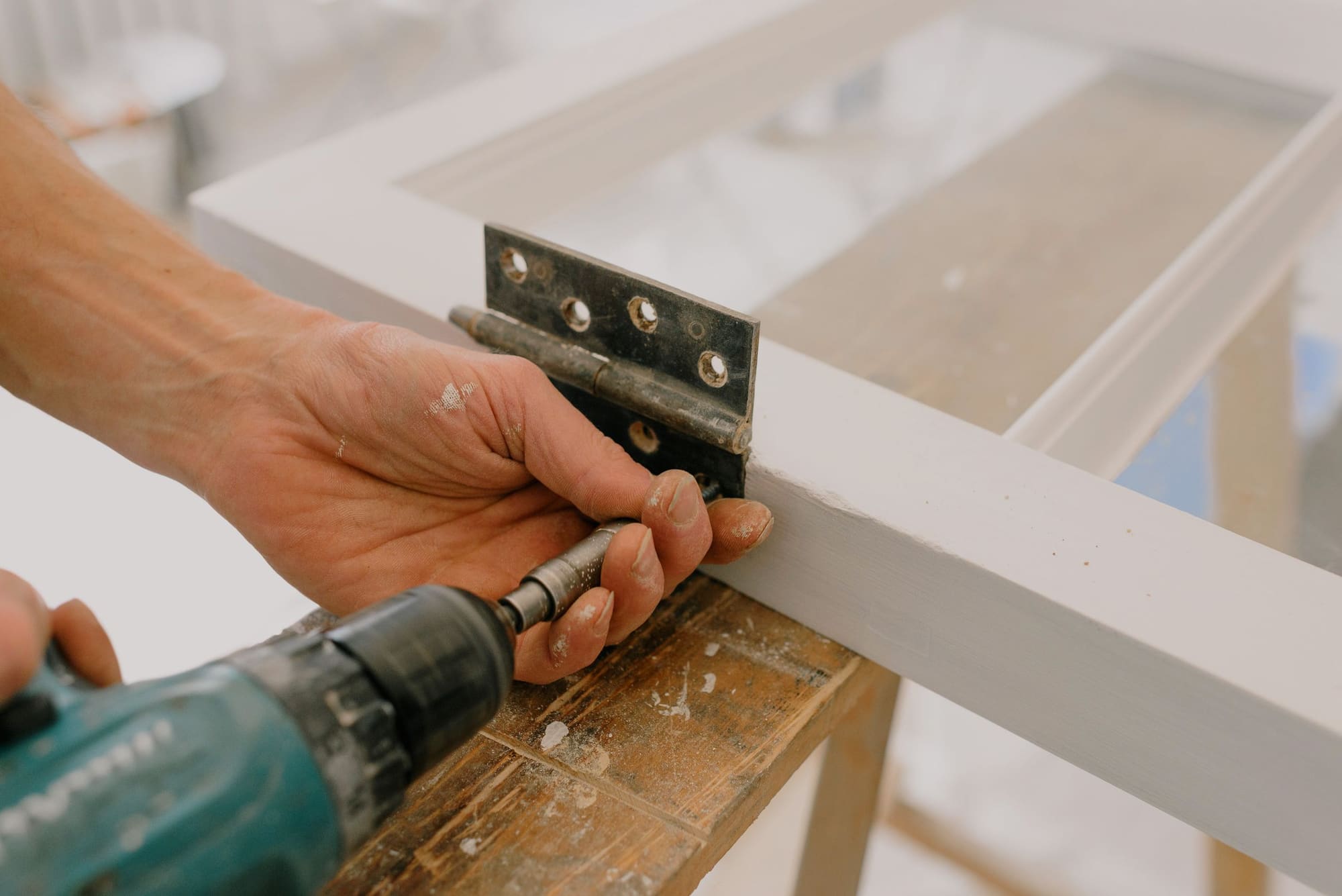 Hands using a drill to fasten a metal hinge to wood